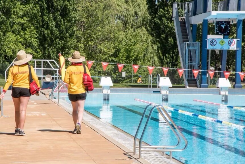 Two lifeguards walking along the edge of a public pool 