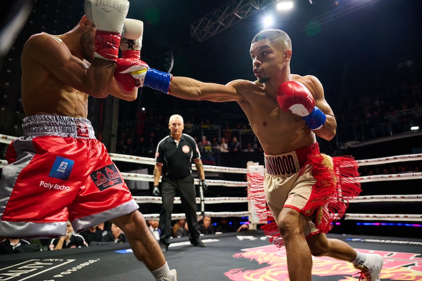 Professional boxer striking opponent in boxing ring as opponent attempts to block 