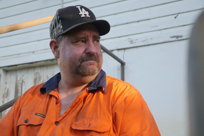 man wearing high-vis work shirt and base ball cap, looking away from the camera with glassy eyes