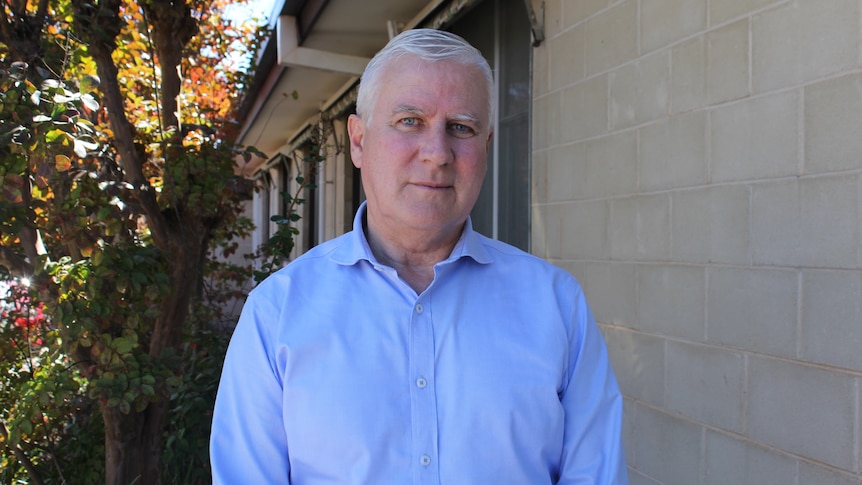 Michael McCormack standing beside a non-descript building, with a tree over his right shoulder.