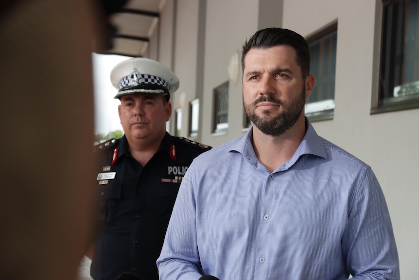 A photo of a man wearing a sky blue shirt with a uniformed officer man in the background.