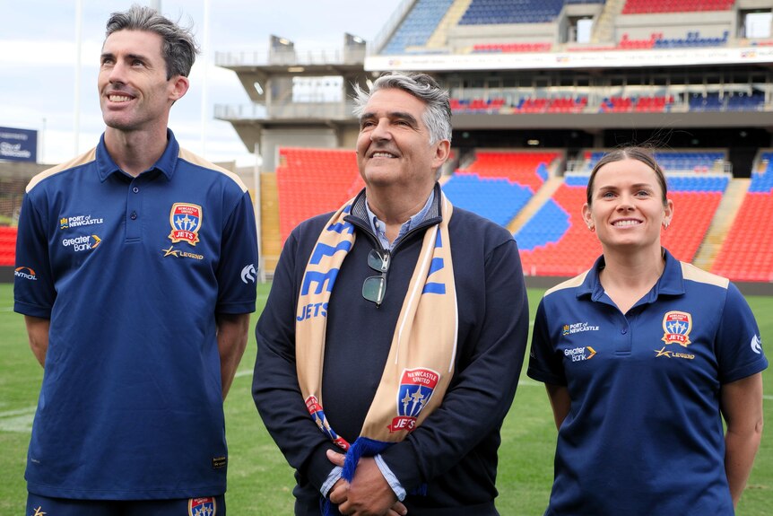 three people stand together at a football stadium