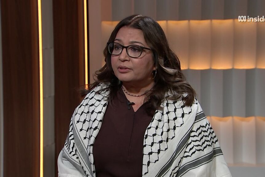 A woman with black-rimmed glasses speaking during a news interview from television studio.