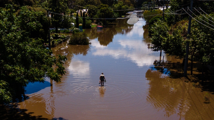 A drone shot looking down at a flooded road as a person in the distance walks through the water covering the road