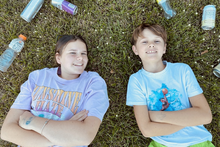 Two kids lying on grass surrounded by empty bottles and cans