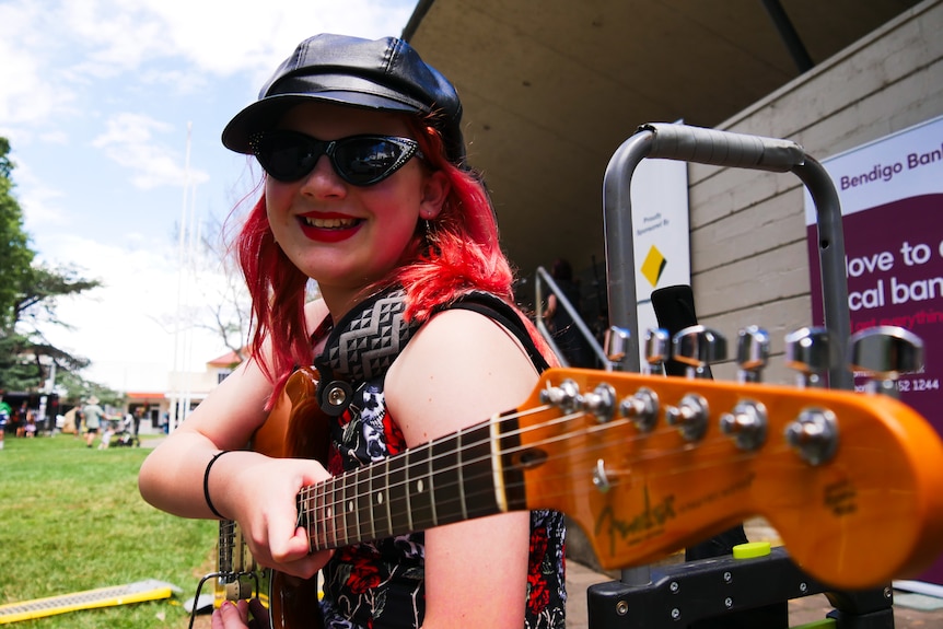 a kid smiles at the camera wearing cool sunnies and a guitar