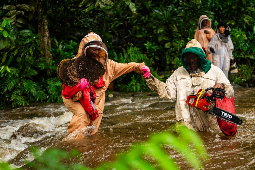 Image of two people crossing a river wearing bee suits.