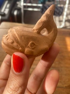 A hand with red nail polish holds a small carved wooden whale. 