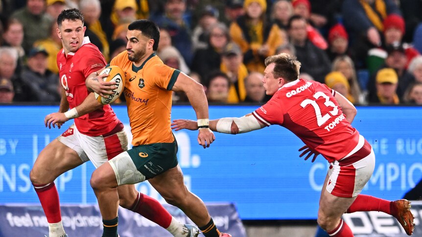 Two rugby men in red chase one rugby man in Australian colours with the ball 