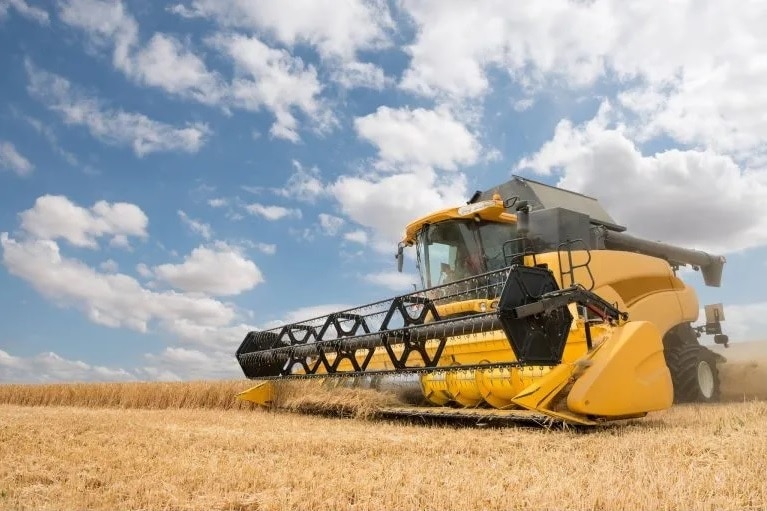 Large yellow combine harvester being driven through a field of wheat.