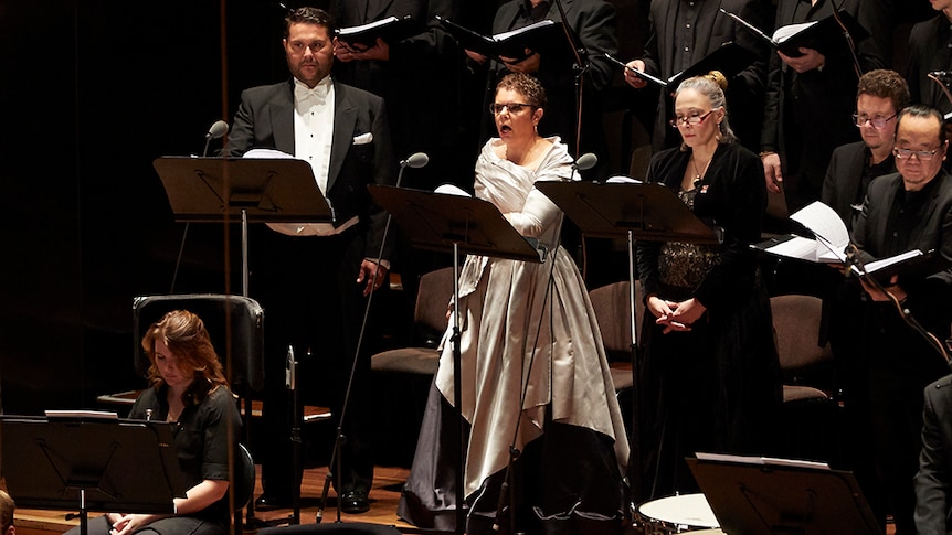 Composer Deborah Cheetham Fraillon sings on stage amongst a choir.