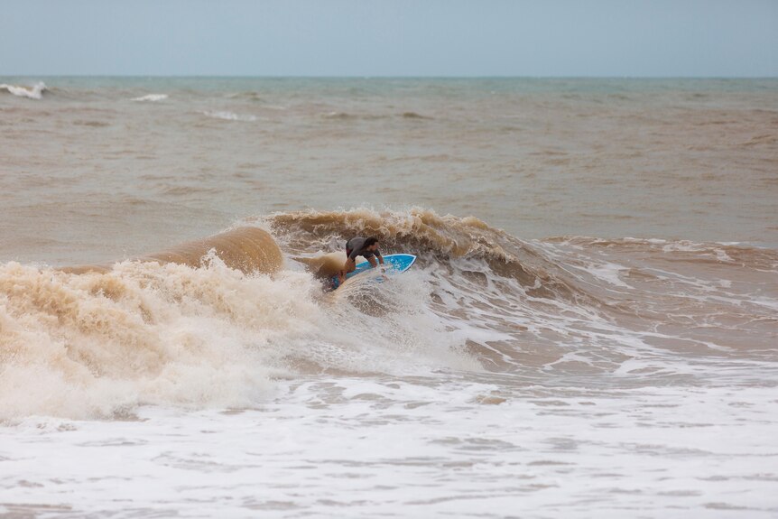 a surfer takes on a wave in the beach that looks brown and dirty