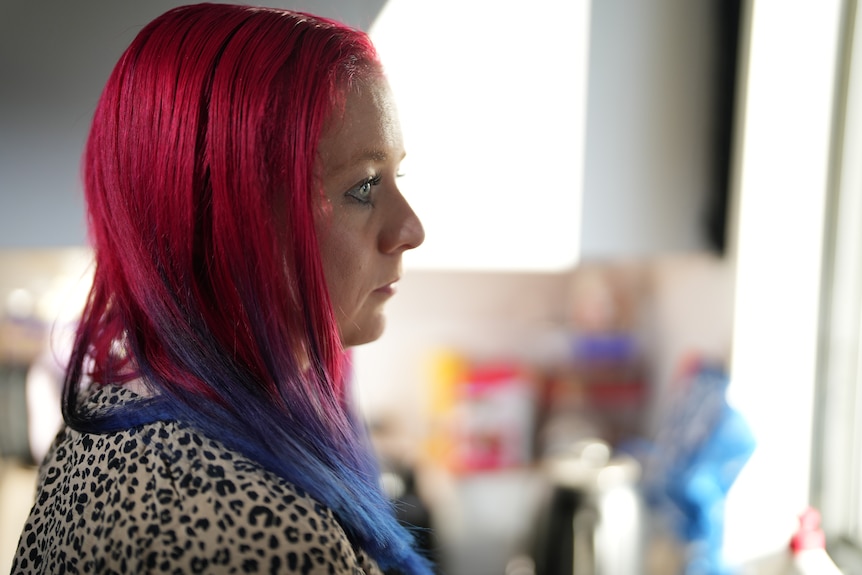 Side portrait of woman with pink and purple hair, wearing a leopard print top.