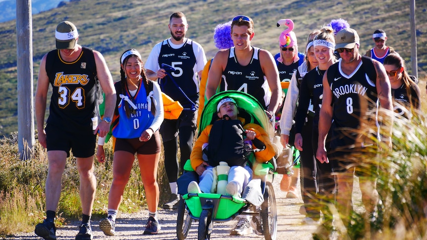 a group of people walk uphill and push a man in a wheelchair.