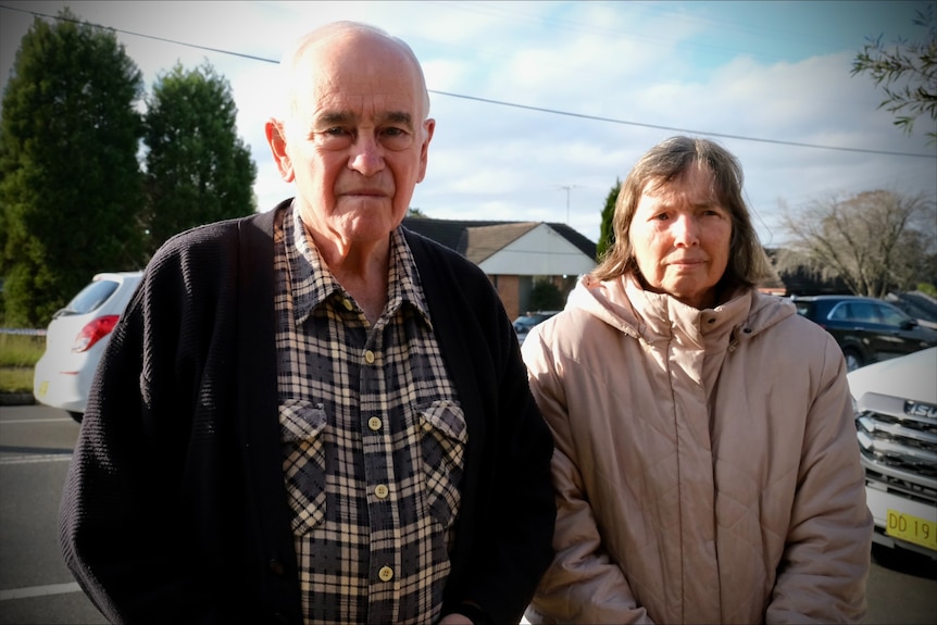 A man and a woman stand outside a burnt out house.