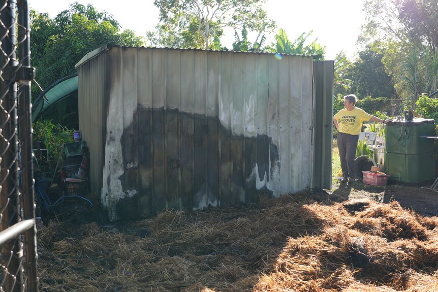 Jaustine Glover stands next to the Karama Community Garden shed that is visibly burnt with a black mark showing on the exterior.