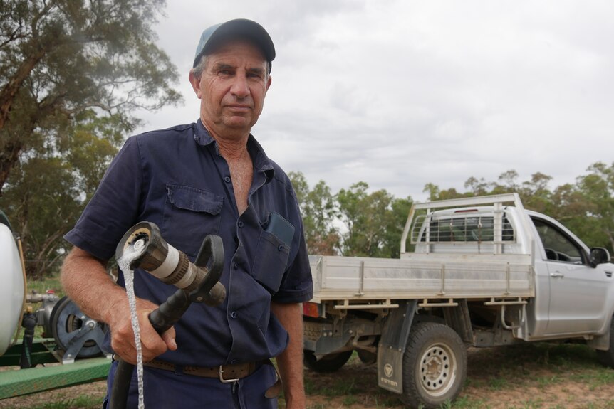 A farmer holding a water hose leaking water.