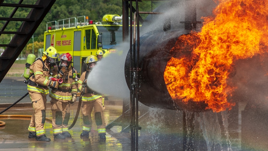 Firefighters aiming a huge torrent of water from a hose at a prop jet engine ablaze.