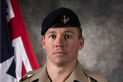 Lance Corporal Jack Fitzgibbon in RAAF uniform with Australian flag behind him in official photo