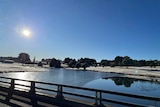 A lake which has iced over. The sun shines brightly overhead. 