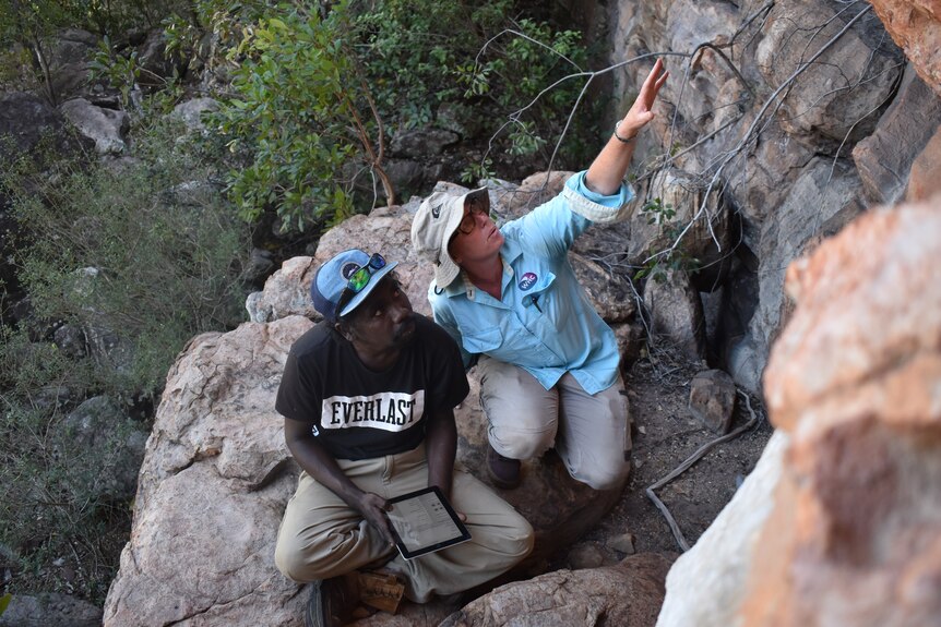 Two people sit on rock high off the ground and looks at rock art 