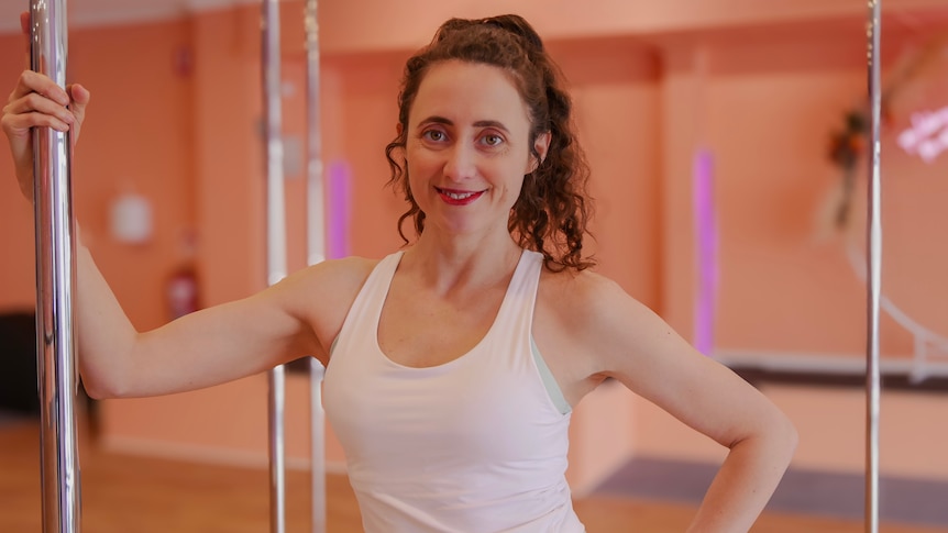 A woman holding on to a dancing pole inside a studio. 