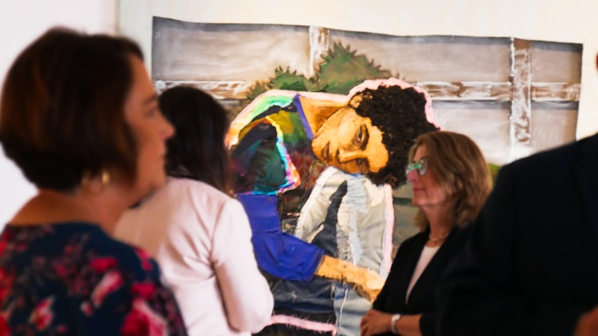 a group of people stand in a gallery with a beautiful piece of art in the background