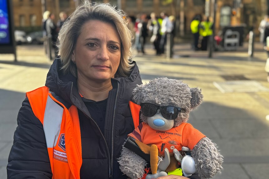 Woman in high-vis orange jacket holding a teddy bear wearing sunglasses