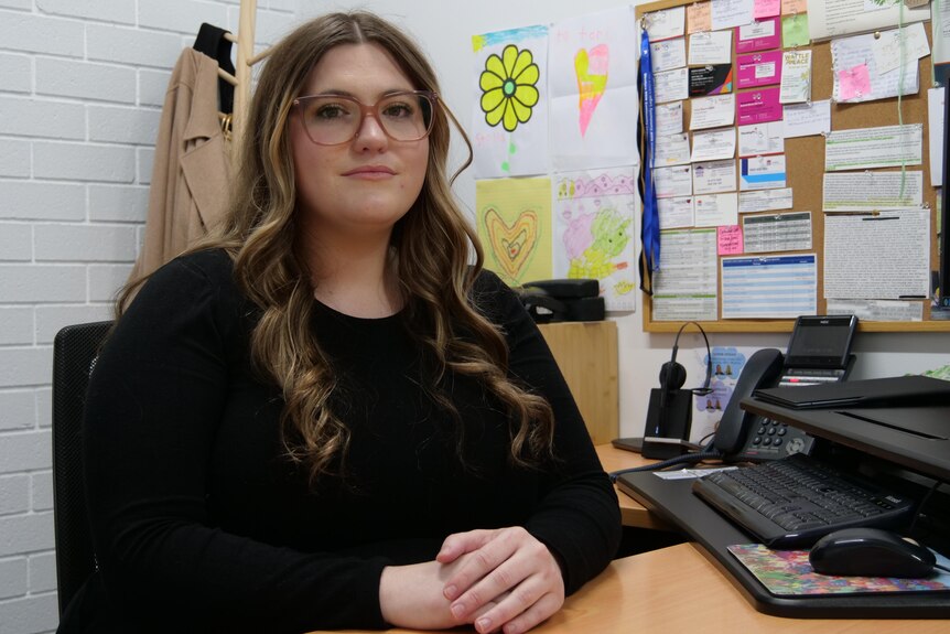 Woman sitting at a desk, staring at a camera. 