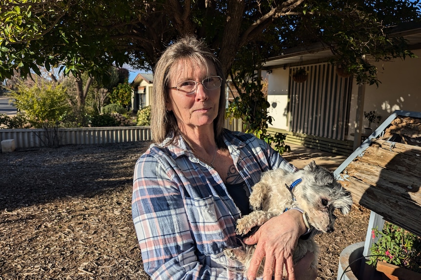 A woman holds a small dog in her arms.