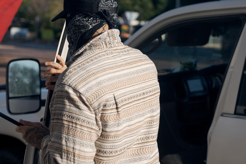 Man wearing bandana across face opens car door