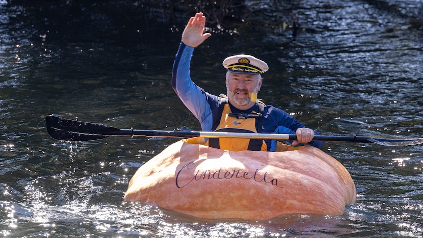 A man dressed as popeye sits in a hollowed out 400 kilo pumpkin waving as he paddles in a river