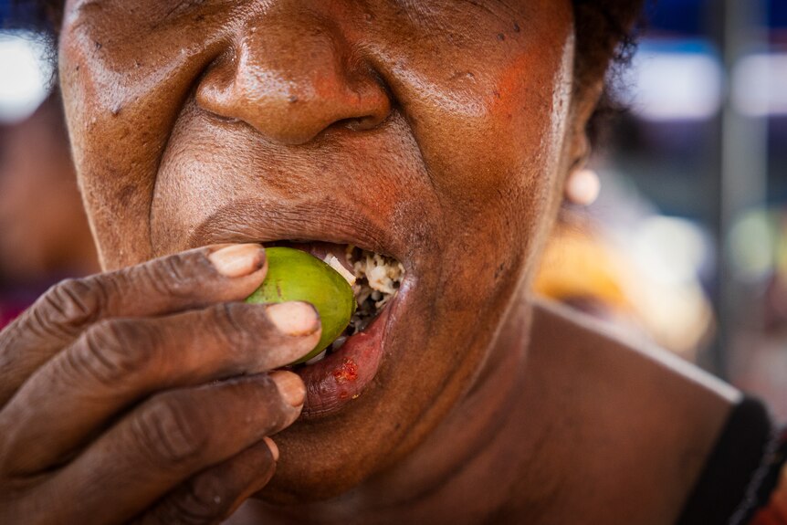 A close-up shows a woman placing a green nut into her mouth