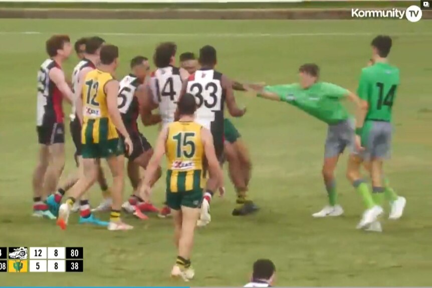 A still from a AFLNT match which shows multiple players standing around, one players arm is holding the shirt of an umpire.