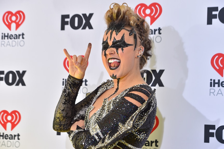 JoJo Siwa poses wearing a black and silver outfit and with black paint decorating parts of her face.