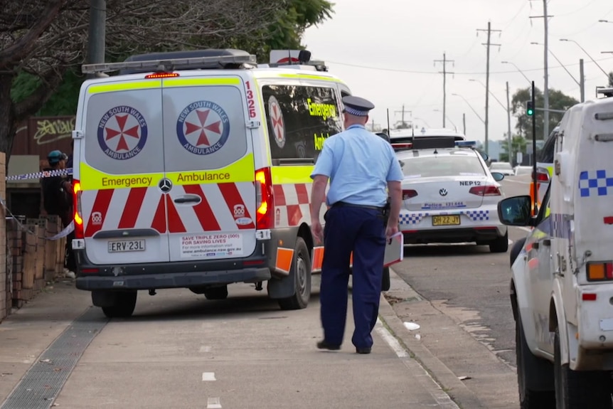 Police officer walking on footpath and ambulance at scene of fatal Kingswood stabbing in Western Sydney