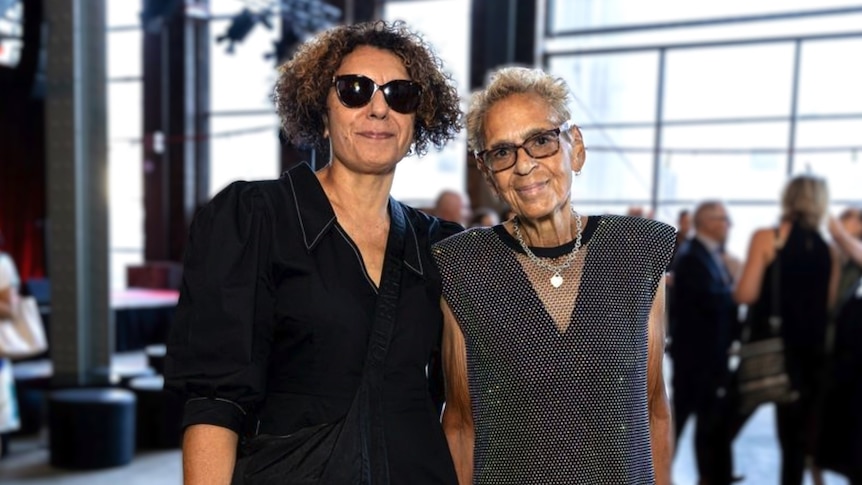 Two older Indigenous women - Janina Harding and Destiny Deacon - standing together at an exhibition opening