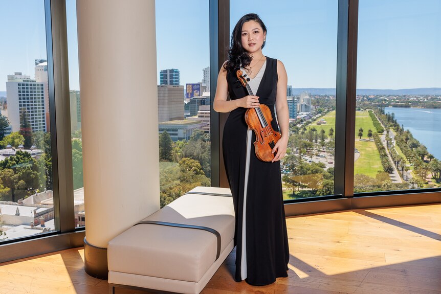 Emily Sun wearing a black evening dress posing with "The Adelaide" violin.