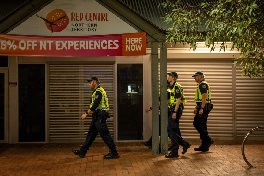 A group of police officers walk down a street in front of a shop front at night 