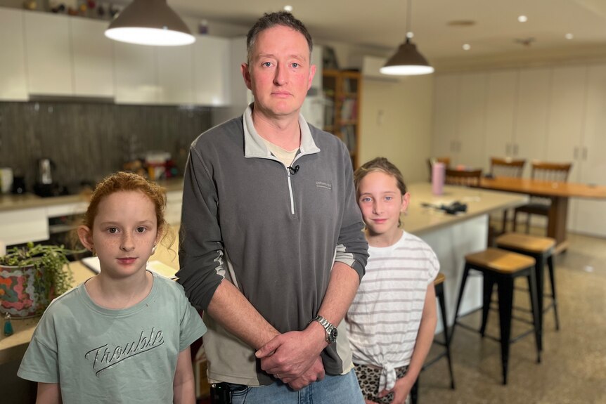 Man standing with two daughters either side with kitchen in background