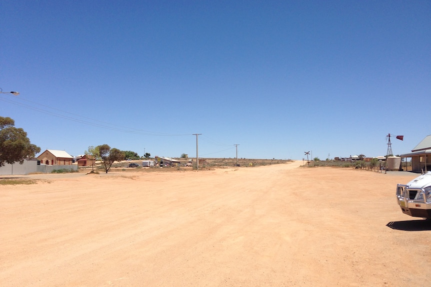 Dirt road with some houses either side.