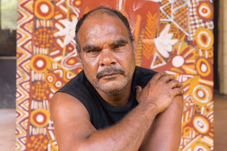 Johnathon Bush leans forward with his arms crossed over in front of one of his artworks. 