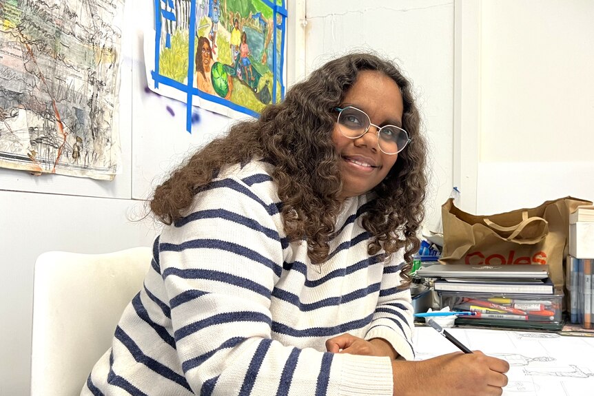 A young woman sits drawing artwork.