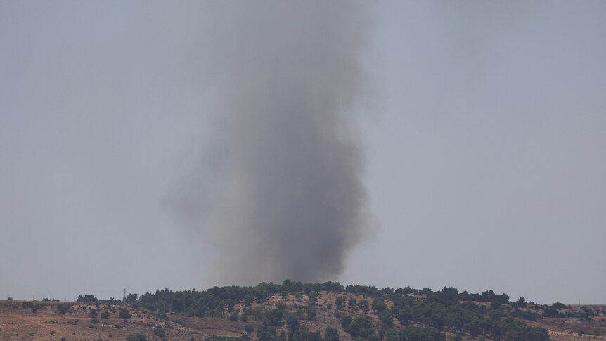 Smoke rises above a grassy hill.