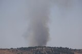 Smoke rises above a grassy hill.