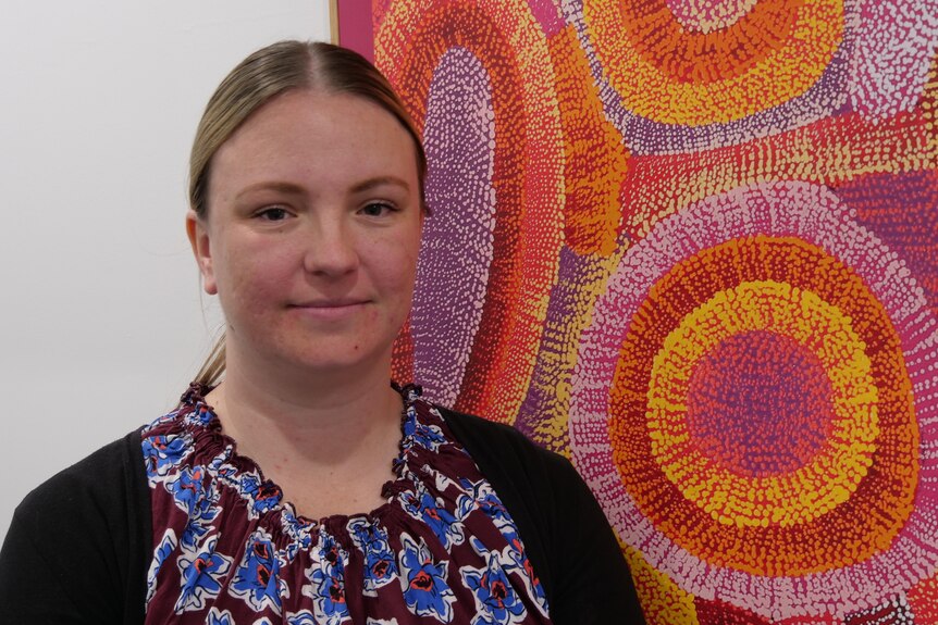 Young woman staring at camera, with artwork in the background.