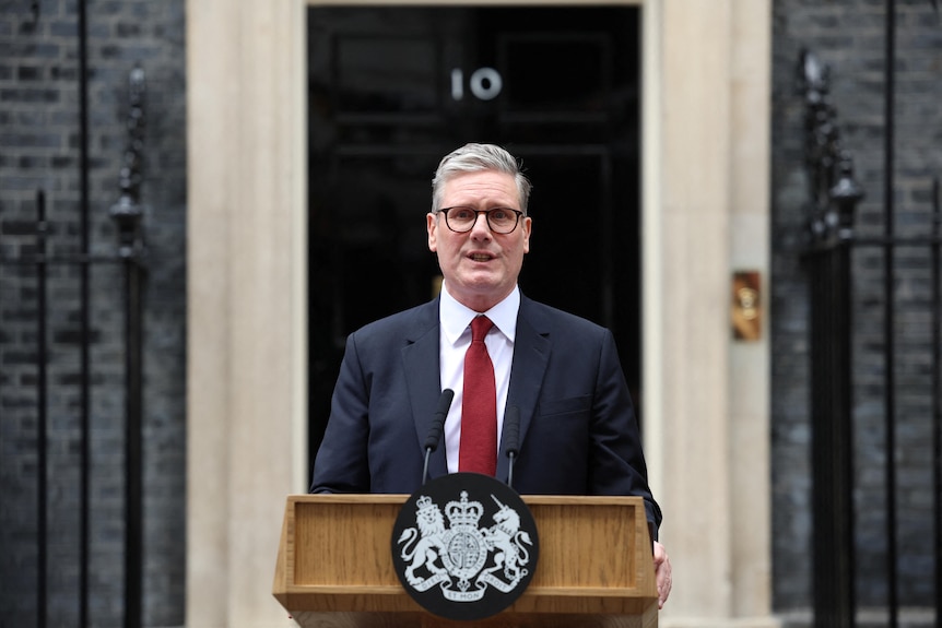 A man in a suit stands in front of a lecturn.