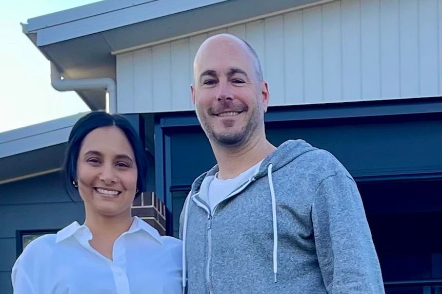 Man and woman smiling, standing side by side in front of their home