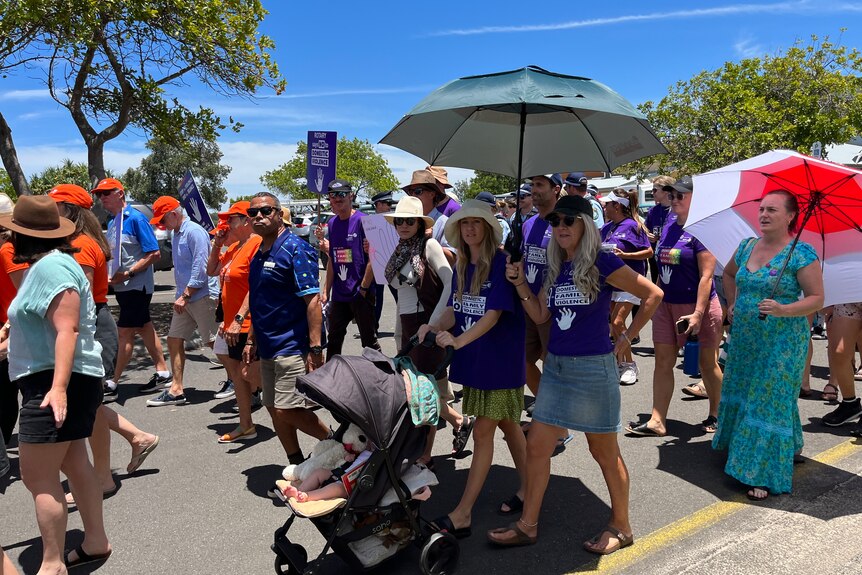 woman pushing a pram alongside her mother and a crowd of people marching