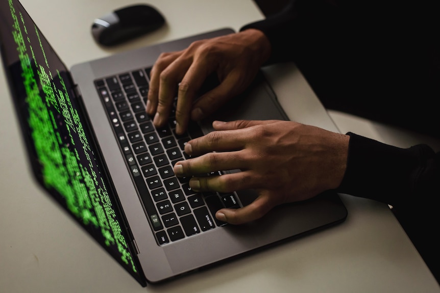 A computer with hacking software on the screen and someone's hands typing on the keyboard